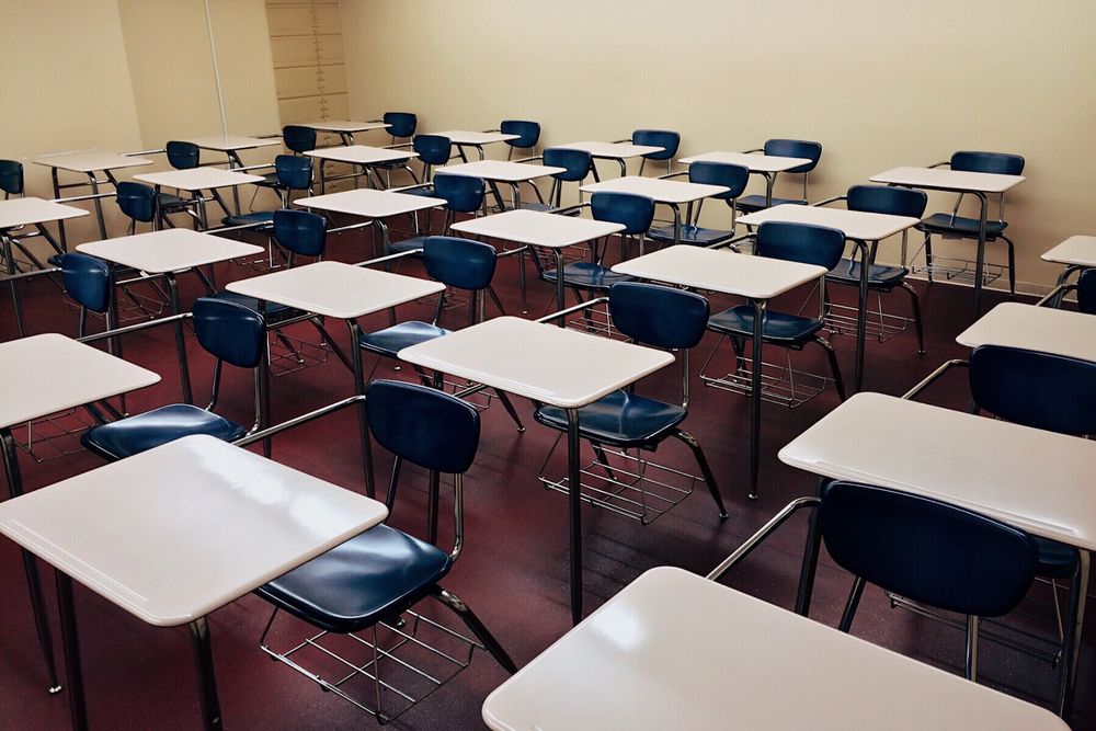 Rows of empty desks and chairs in a classroom.